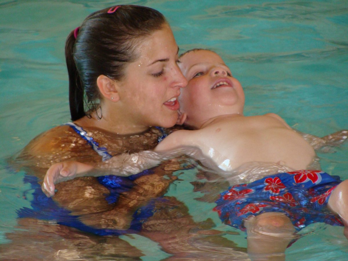An adult supporting a young child during a swimming lesson in a pool.